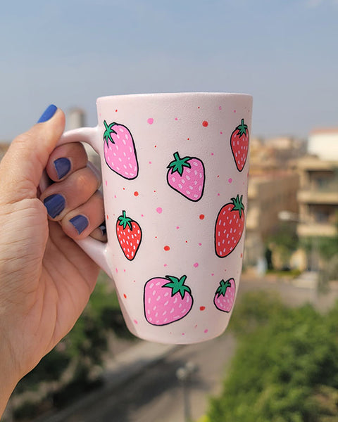 A pastel pink hand painted mug with strawberries in red and pink and red and pink dots, all scattered all over the mug