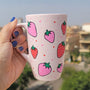 A pastel pink hand painted mug with strawberries in red and pink and red and pink dots, all scattered all over the mug