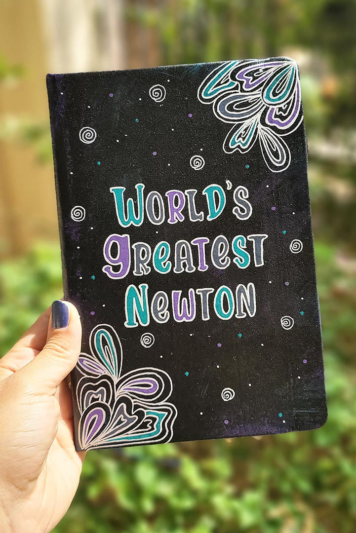 A Black galaxy hand painted notebook with doodles coming from 2 side corners and the words "World's greartest newton" in the center with small swirls scattered all over