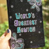 A Black galaxy hand painted notebook with doodles coming from 2 side corners and the words 