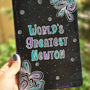 A Black galaxy hand painted notebook with doodles coming from 2 side corners and the words "World's greartest newton" in the center with small swirls scattered all over