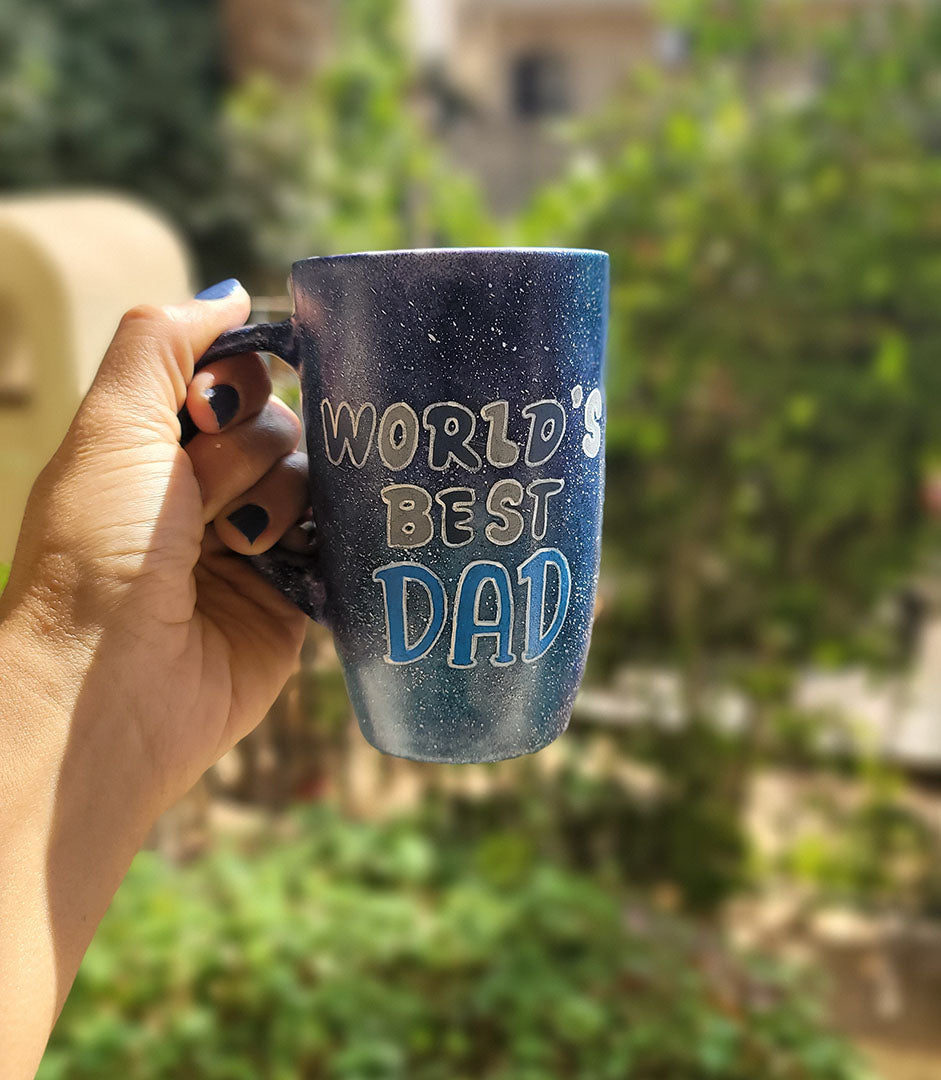 A black galaxy hand painted mug with the sentence "Worlds Best dad"