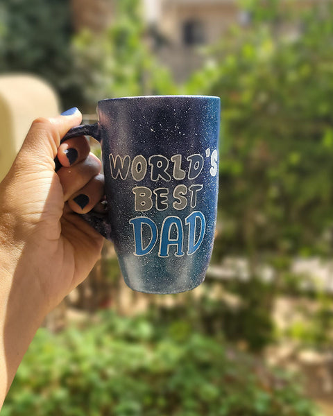 A black galaxy hand painted mug with the sentence "Worlds Best dad"