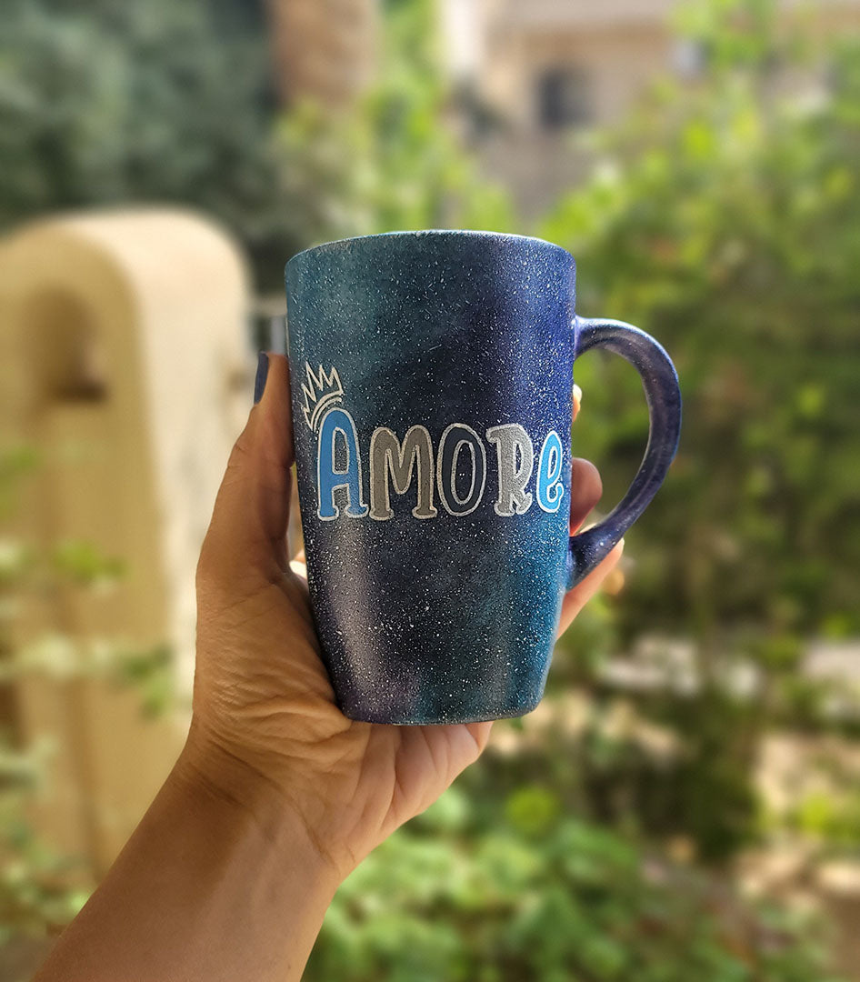 A black galaxy hand painted mug with the name "Amore" and a little crown on the letter A