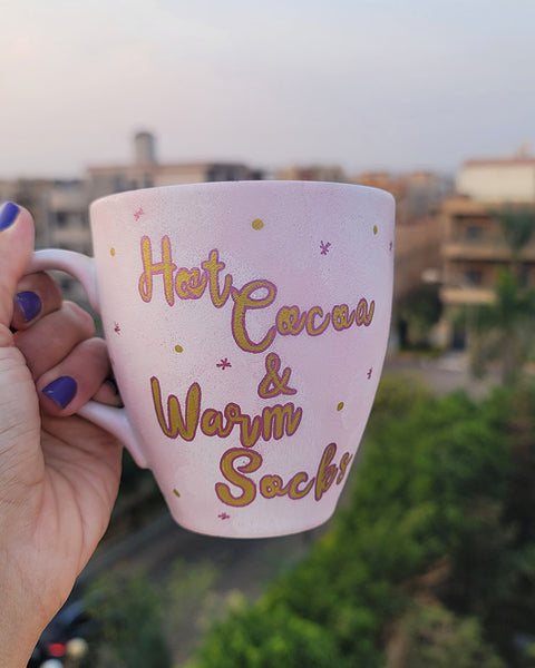 A Hand painted Baby Pink mug with the sentence "Hot Cocoa and warm socks" in gold