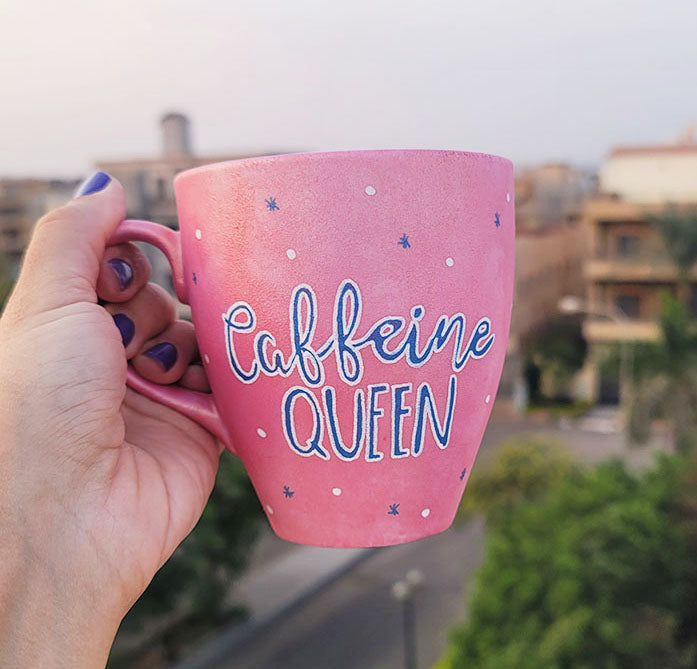 A Hand - painted shimmery pink mug with the words "Caffeine Queen" in blue