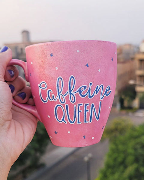 A Hand - painted shimmery pink mug with the words "Caffeine Queen" in blue