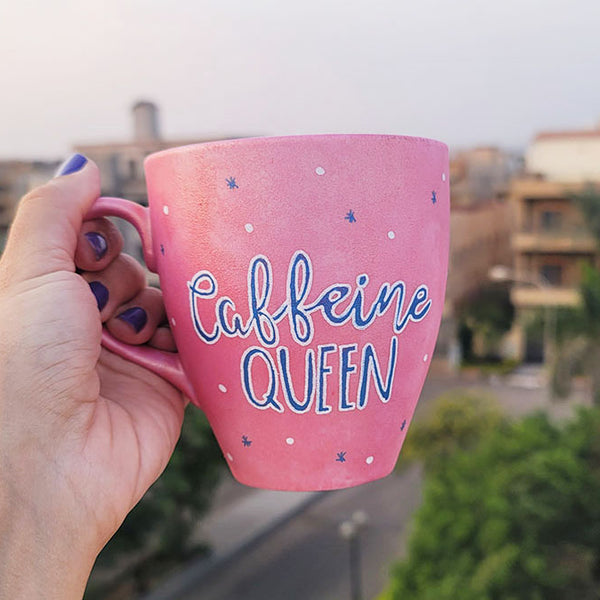 A Hand - painted shimmery pink mug with the words "Caffeine Queen" in blue