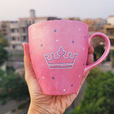 A Hand - painted shimmery pink mug with A Crown painted in blue