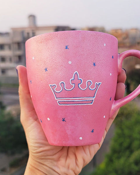 A Hand - painted shimmery pink mug with A Crown painted in blue