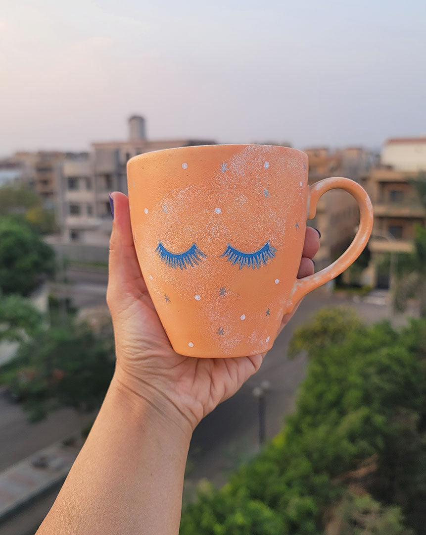 A Baby Orange Hand-painted mug with 2 closed eyes with lashes