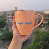 A Baby Orange Hand-painted mug with 2 closed eyes with lashes