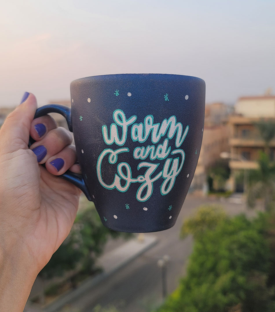 A Shimmery blue hand painted mug with the words "Warm and Cozy " in silver