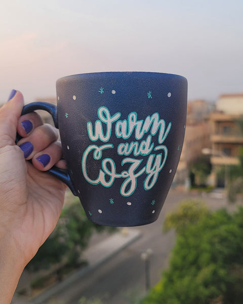 A Shimmery blue hand painted mug with the words "Warm and Cozy " in silver