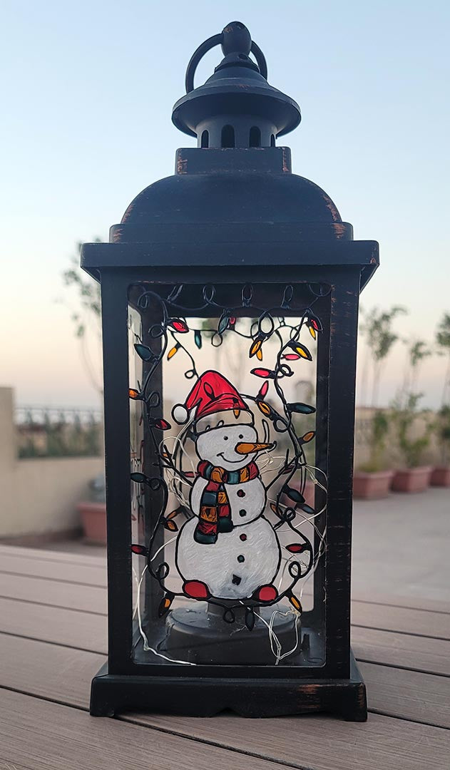 A Black Vintage Lantern with a snowman painted on the glass and festive lights above him