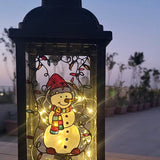 A Black Vintage Lantern with a snowman painted on the glass and festive lights above him, shown at night when the lantern lights are on