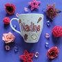 A Baby Blue hand painted mug with the name nadine and chocolate bars, tooth, toothbrush and chocolate pieces scattered all over.