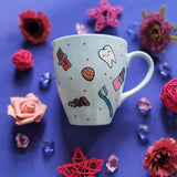 A Baby Blue hand painted mug with chocolate bars, tooth, toothbrush and chocolate pieces scattered all over.