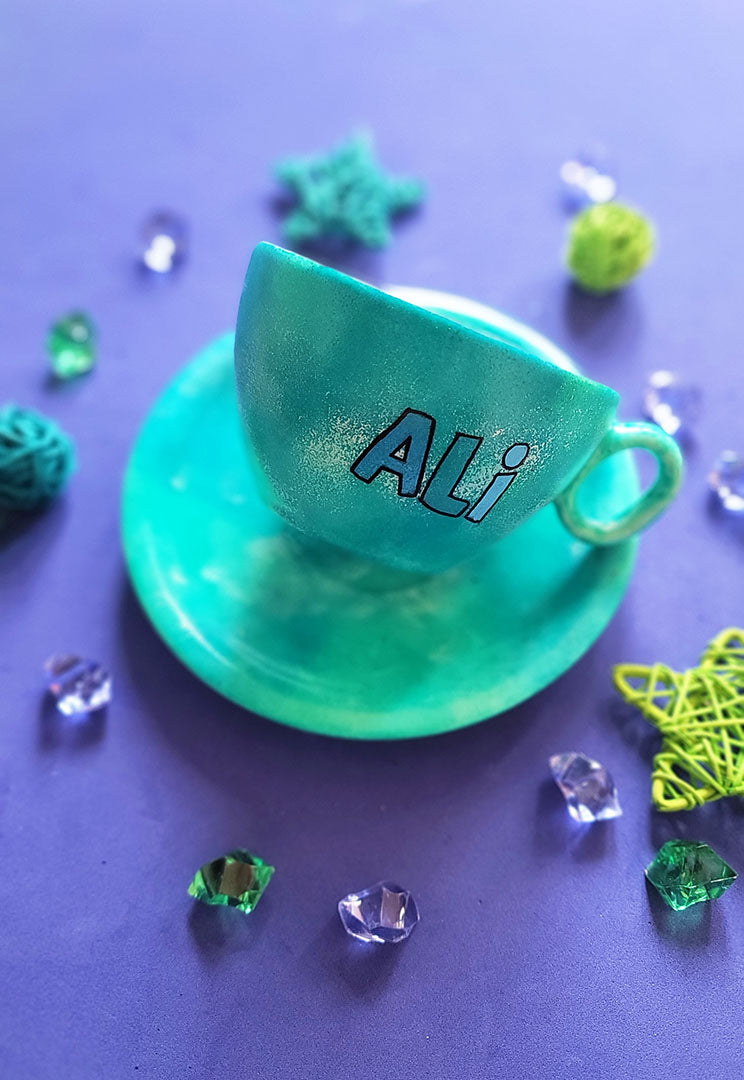 A green galaxy hand painted cup and saucer with the name "Ali"