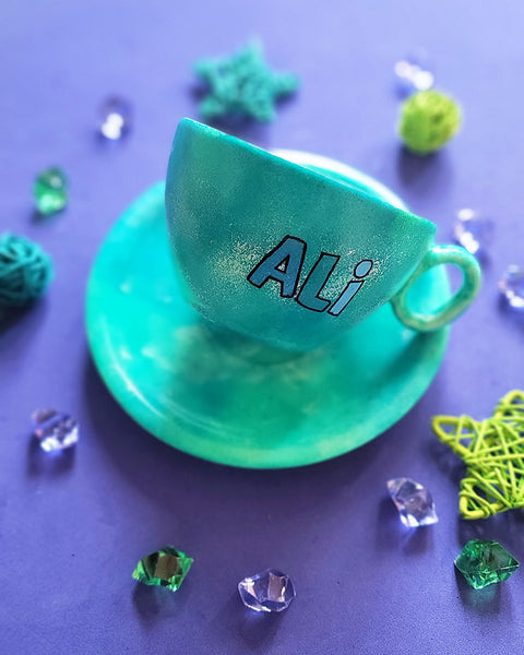 A green galaxy hand painted cup and saucer with the name "Ali"