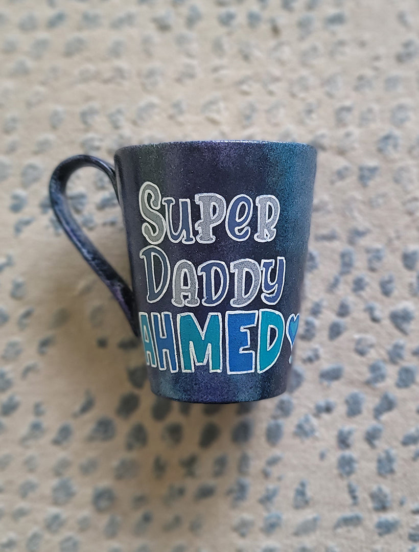 A dark Sky Hand painted mug with the words "Super Daddy Ahmed " and a heart