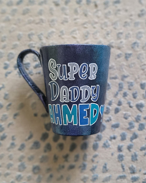 A dark Sky Hand painted mug with the words "Super Daddy Ahmed " and a heart