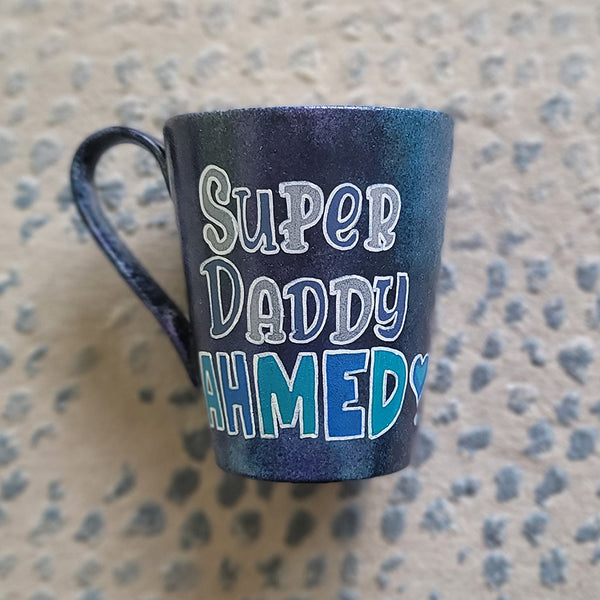 A dark Sky Hand painted mug with the words "Super Daddy Ahmed " and a heart