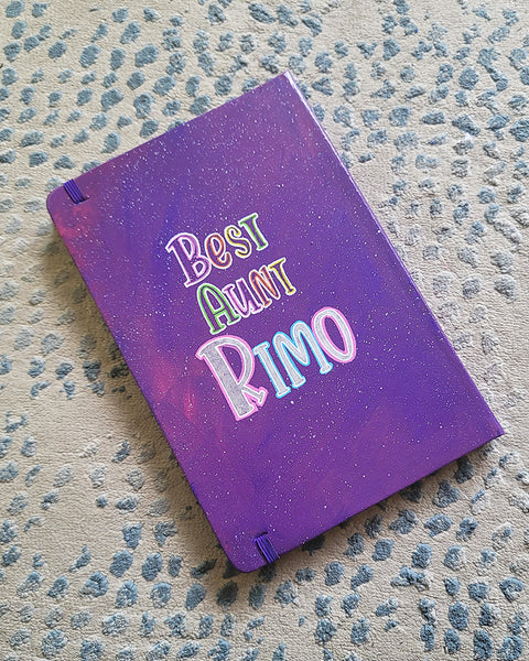 A Purple Galaxy Hand painted notebook with the words "Best Aunt Rimo"