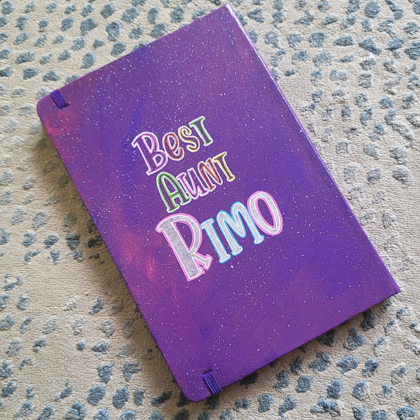 A Purple Galaxy Hand painted notebook with the words "Best Aunt Rimo"