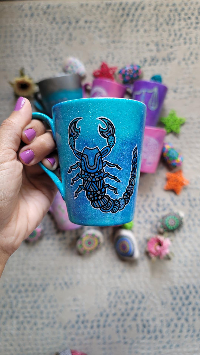 A blue galactic mug with a Scorpio zodiac sign hand-painted on it