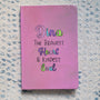 A Pastel Pink Hand painted Notebook with the name Dina wirtten on top and under it the sentence "the bravest heart and kindest Soul" all wirtten in black and colored in purple, pink, green and blue.