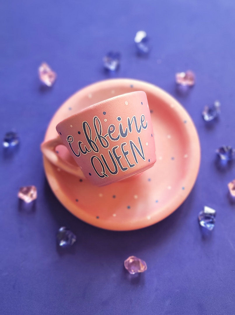 A Hand - painted shimmery pink cup and saucer with the words "Caffeine Queen" in blue and white and blue dots scattered all over