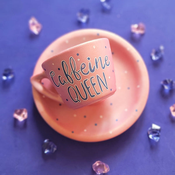 A Hand - painted shimmery pink cup and saucer with the words "Caffeine Queen" in blue and white and blue dots scattered all over