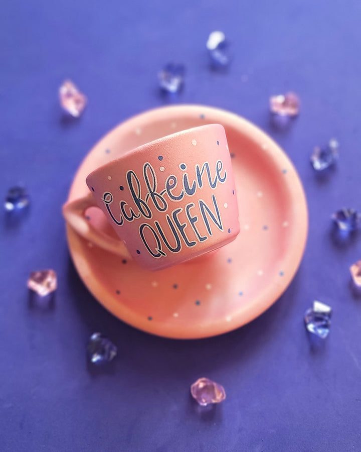 A Hand - painted shimmery pink cup and saucer with the words "Caffeine Queen" in blue and white and blue dots scattered all over