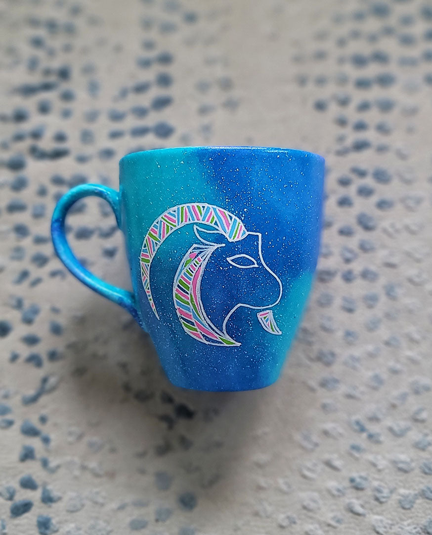 A Hand-painted blue galaxy mug with Capricorn sign in white and colored with patterns of pink,blues and greens