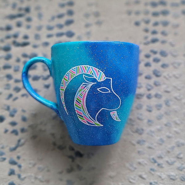 A Hand-painted blue galaxy mug with Capricorn sign in white and colored with patterns of pink,blues and greens