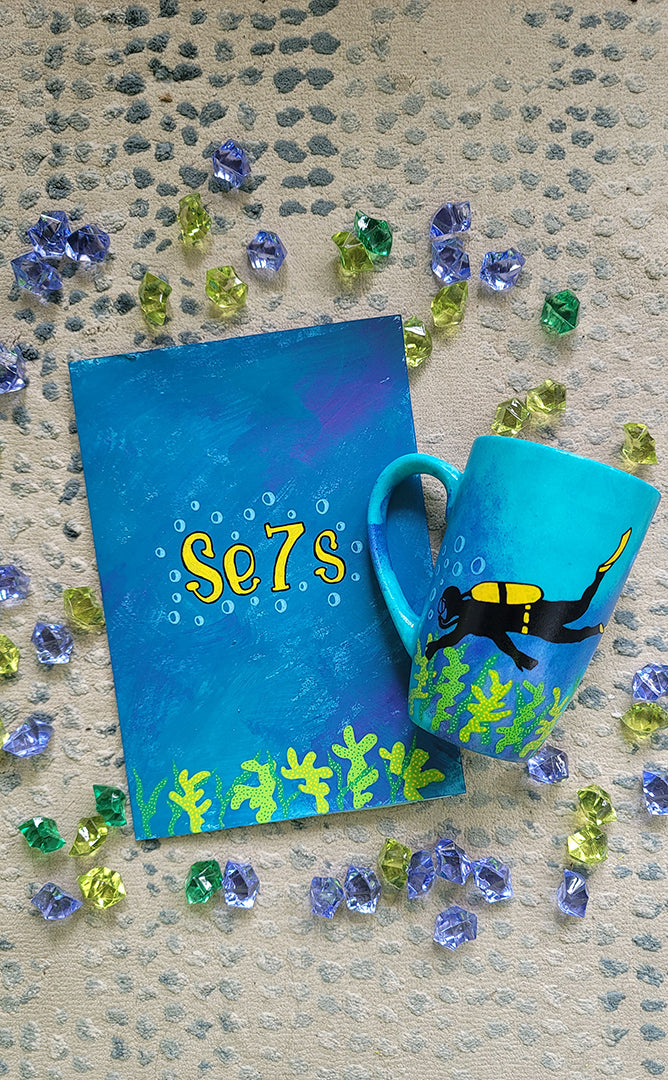 A Gift Set of a mug and matching card all in blue galaxy color and with coral reefs on the bottom. the card has the name Se7s and the mug has a diver 