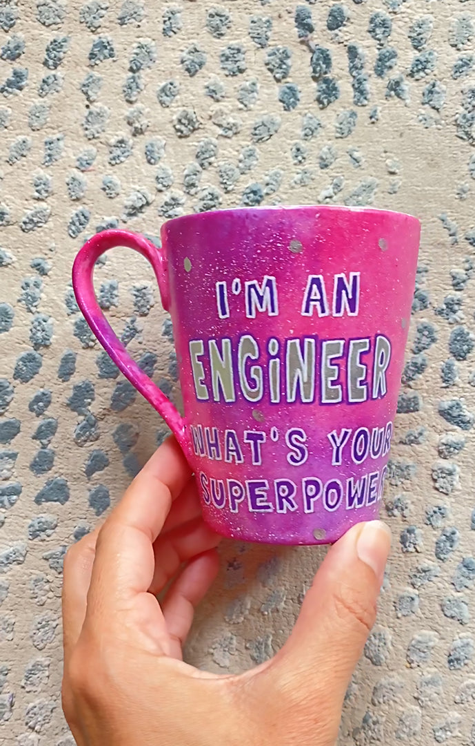 A Pink galaxy hand painted mug with the sentence "I'm and Engineer what your superpower"