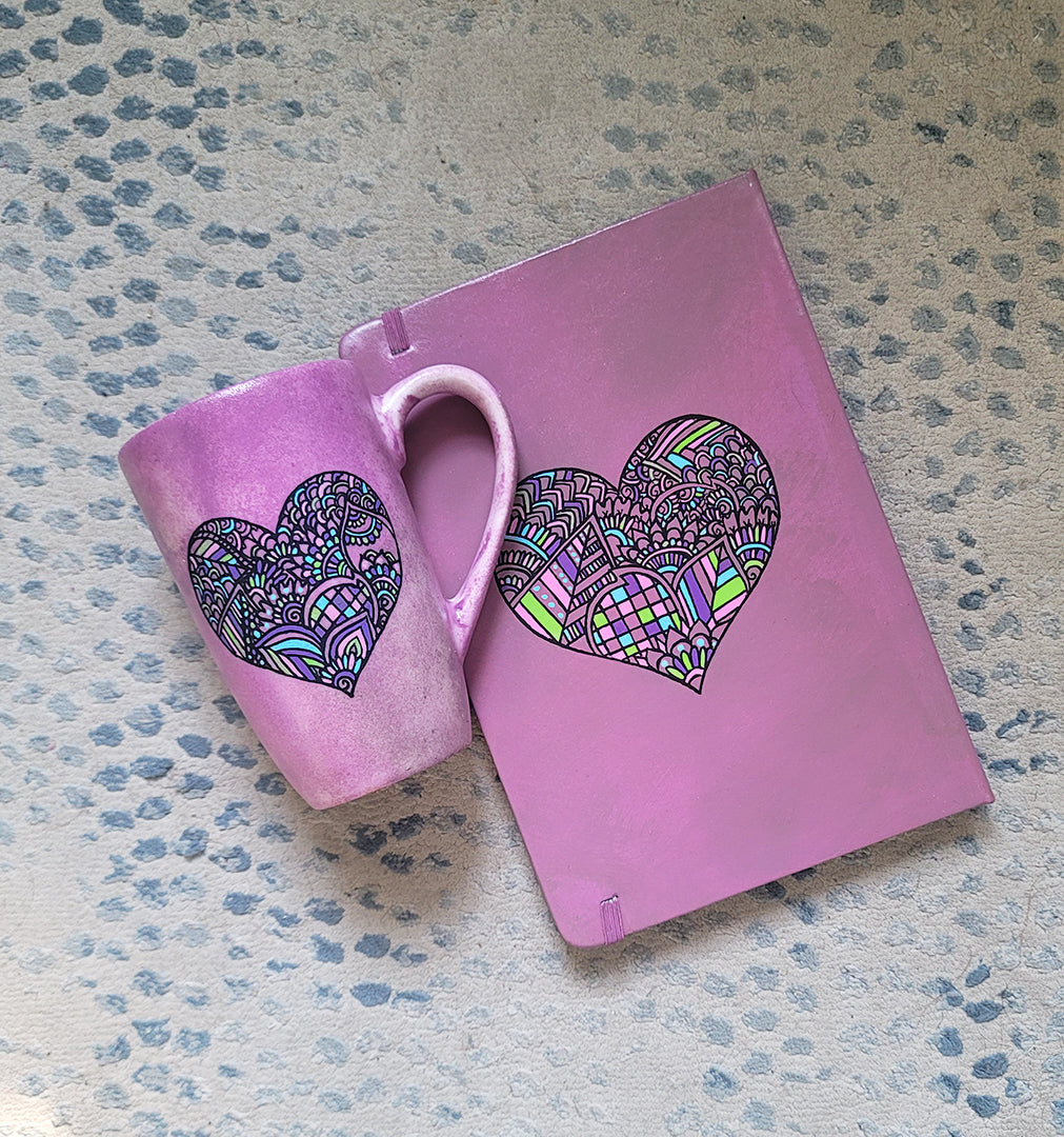 a Pastel Pink hand painted Gift Set of a mug and notebook both with a heart drawn in black and filled with colorful patterns