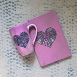 a Pastel Pink hand painted Gift Set of a mug and notebook both with a heart drawn in black and filled with colorful patterns