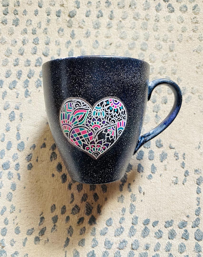 a Black Galaxy hand painted mug with a heart drawn in white filled with colorful patterns