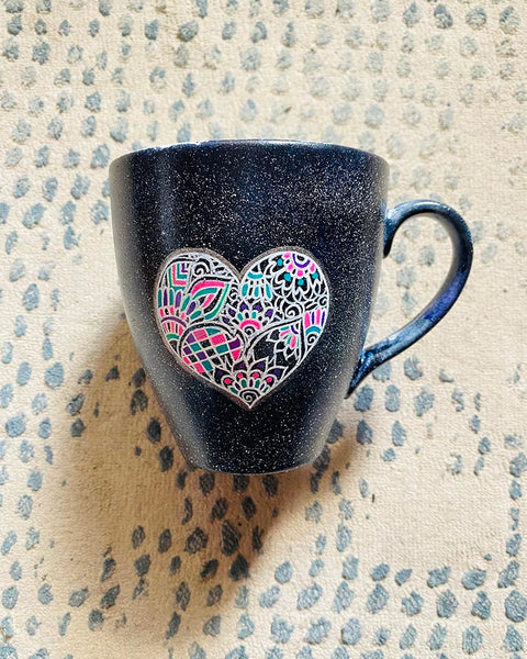 a Black Galaxy hand painted mug with a heart drawn in white filled with colorful patterns