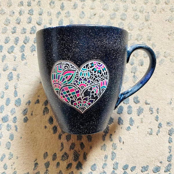 a Black Galaxy hand painted mug with a heart drawn in white filled with colorful patterns