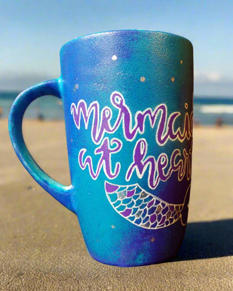 A blue hand painted mug with the words "Mermaid at heart" with a mermaid tail painted below it