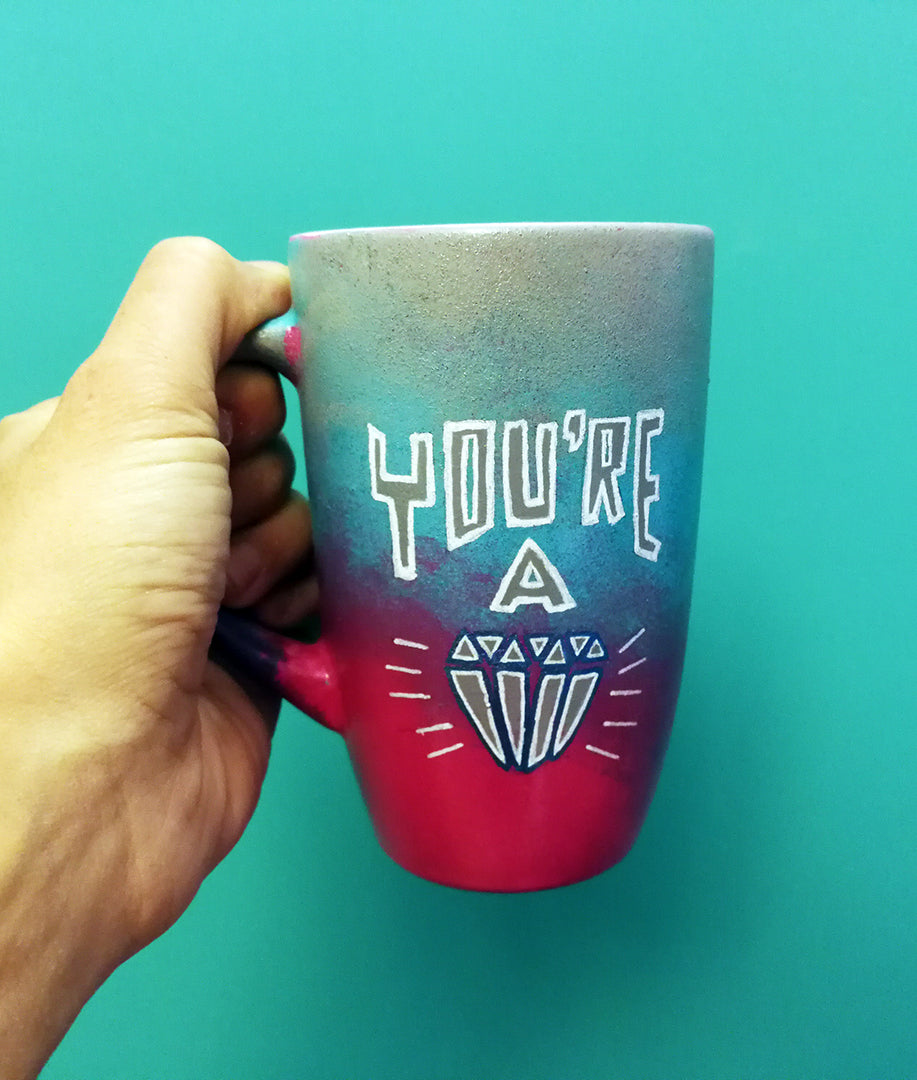 A Gradient colored mug(grey, blue and fushia) with the words "You're A" and a diamond painted below it