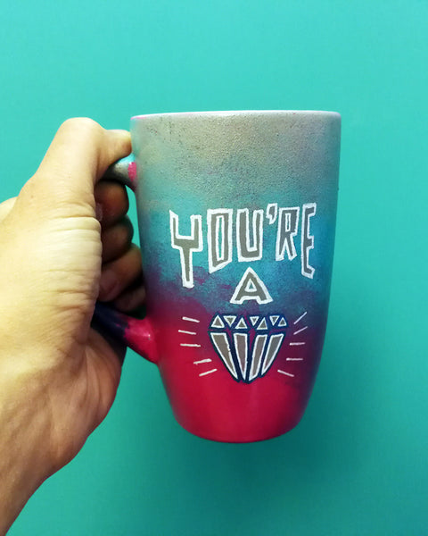 A Gradient colored mug(grey, blue and fushia) with the words "You're A" and a diamond painted below it