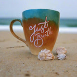 A gradient colored hand painted mug (from sand color at the botom to the sea color on top) with the words 