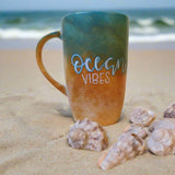 A gradient colored hand apinted mug (from sand color at the botom to the sea color on top) with the words 