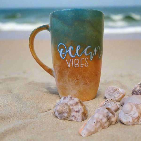 A gradient colored hand apinted mug (from sand color at the botom to the sea color on top) with the words "Ocean Vibes"