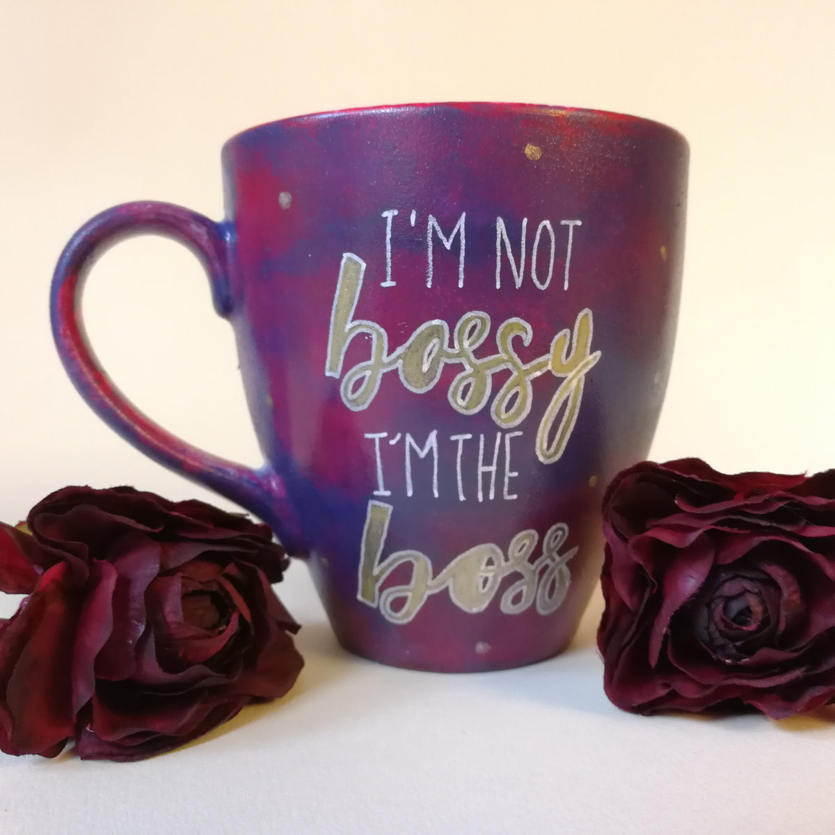 A reddish purple hand painted mug with the words "I'm not bossy , I'm the boss" with the words boss in gold and gold dots scattered all over